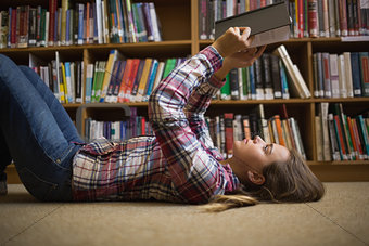 Pretty student lying on library floor reading book