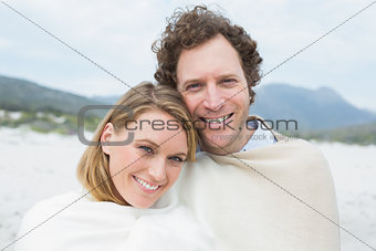Smiling couple wrapped in blanket at beach