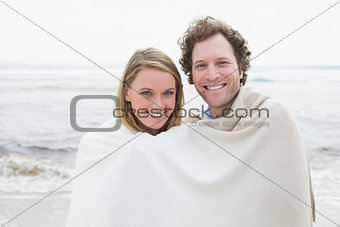 Smiling couple wrapped in blanket at beach