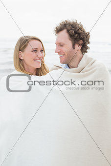 Couple wrapped in blanket at beach