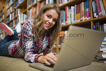 Young smiling student lying on library floor using laptop