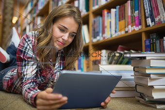 Young pretty student lying on library floor using tablet