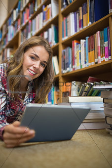 Young happy student lying on library floor using tablet