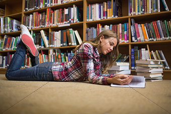 Young student lying on library floor reading