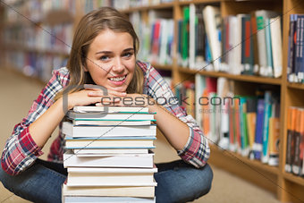 Smiling student sitting on library floor leaning on pile of books