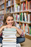 Happy student sitting on library floor leaning on pile of books