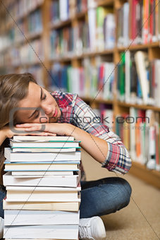 Napping student sitting on library floor leaning on pile of books