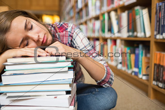 Dozing student sitting on library floor leaning on pile of books