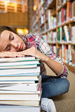 Dozing young student sitting on library floor leaning on pile of books