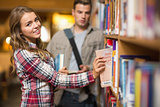Happy student taking book from shelf in library