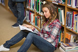 Happy student reading book on library floor