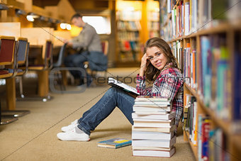 Pretty smiling student reading book on library floor