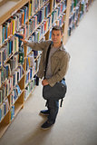 Student taking a book from shelf in library smiling at camera