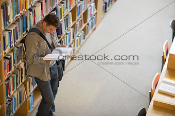 Student reading a book from shelf standing in library