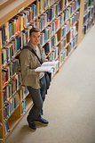 Student reading a book standing in library smiling at camera