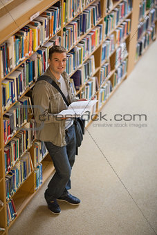 Student reading a book standing in library smiling at camera