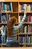 Redhead student taking book from shelf in library