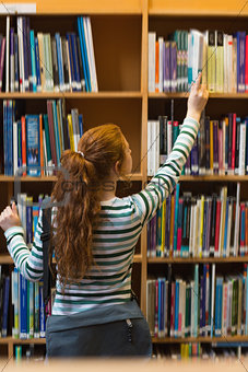 Redhead student taking book from shelf in library