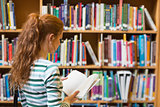Redhead student reading book from shelf in library