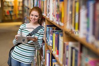 Smiling student reading book leaning on shelf in library