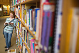 Focused student reading book leaning on shelf in library