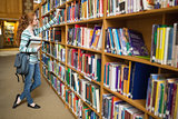 Redhead student taking book from shelf in the library