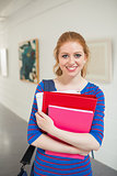 Smiling student holding folders in the hall looking at camera