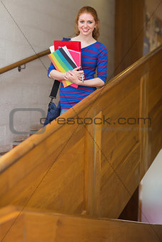Cheerful student holding folders on the stairs looking at camera