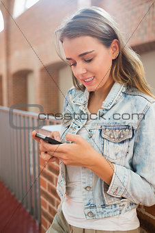 Cheerful student standing in the hall sending a text