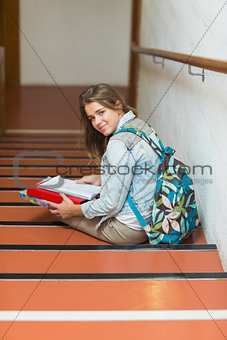 Cheerful young student sitting on stairs looking up at camera