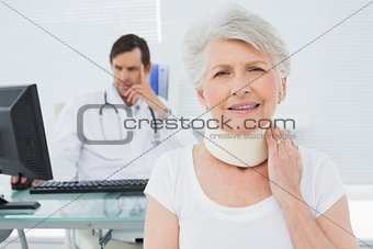 Senior patient in surgical collar with doctor in background at office