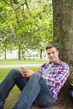 Happy student sending a text outside leaning on tree