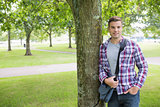 Smiling student leaning on tree looking at camera