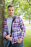Handsome student leaning on tree looking at camera