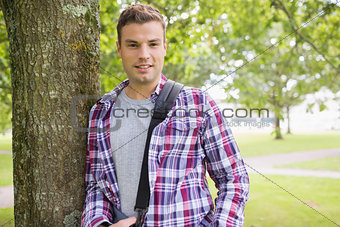 Handsome young student leaning on tree looking at camera