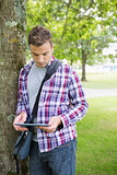 Focused student leaning on tree using his tablet pc