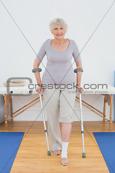 Portrait of a smiling senior woman with crutches in hospital gym