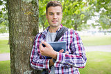 Smiling student leaning on tree holding his digital tablet