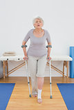 Full length of a senior woman with crutches in hospital gym