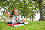Happy young student lying on the grass studying