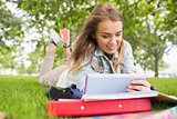 Happy student lying on the grass studying with her tablet pc