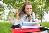 Smiling student lying on the grass studying with her tablet pc