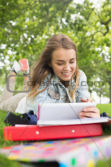 Pretty student lying on the grass studying with her tablet pc