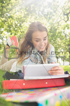 Pretty young student lying on the grass studying with her tablet pc