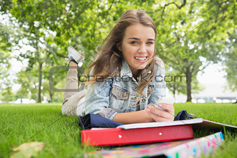 Young smiling student lying on the grass sending a text
