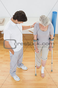 Male therapist assisting disabled senior patient to walk