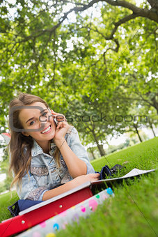 Young smiling student lying on the grass on the phone