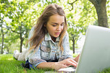Young pretty student lying on the grass using laptop
