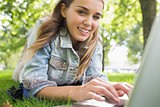 Young smiling student lying on the grass using laptop