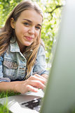 Young smiling student lying on the grass using her laptop
